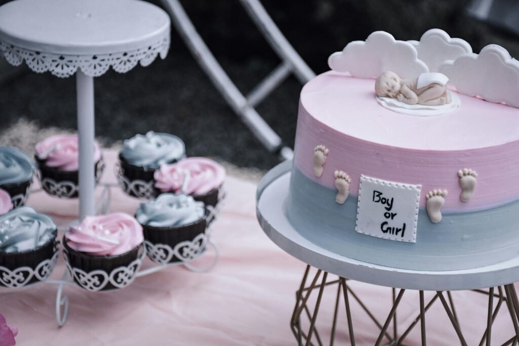 A gender reveal cake with baby decor and pink and blue cupcakes on a stand, perfect for celebrations.