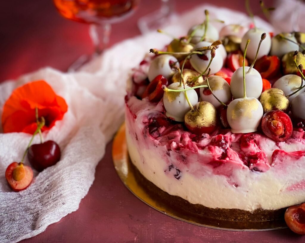 A luxurious cherry cheesecake topped with golden white chocolate drizzled cherries on a rustic tabletop.