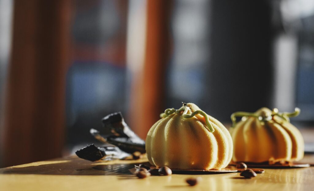 Delicious pumpkin-shaped pastries on a table with coffee beans, capturing a warm and inviting atmosphere.